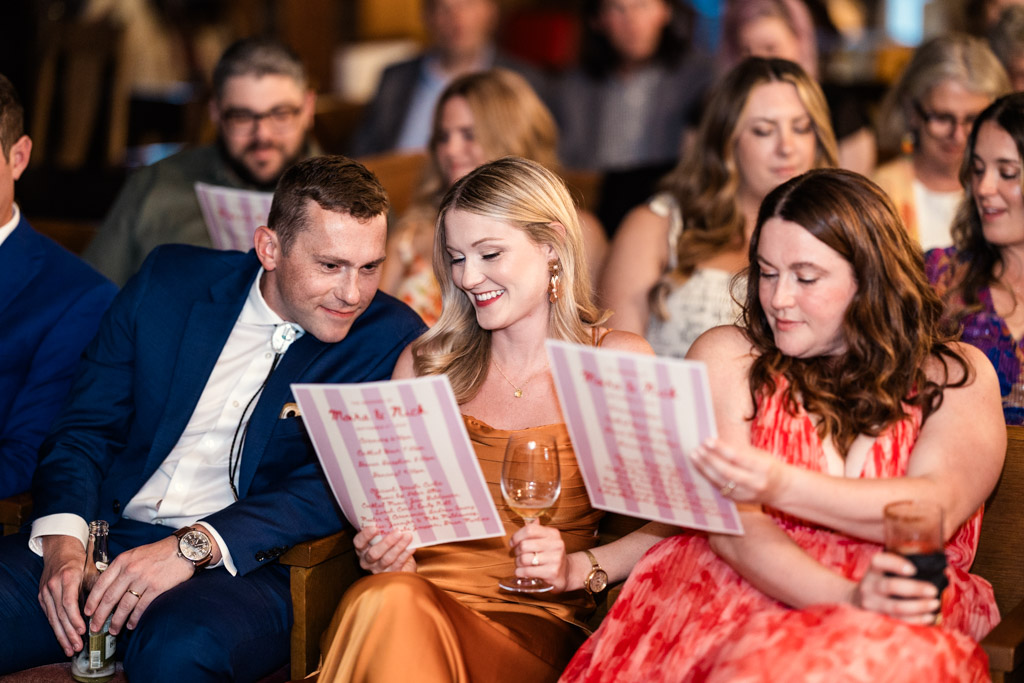 Guests sit together, smiling and reading the wedding program at a Salvage One wedding