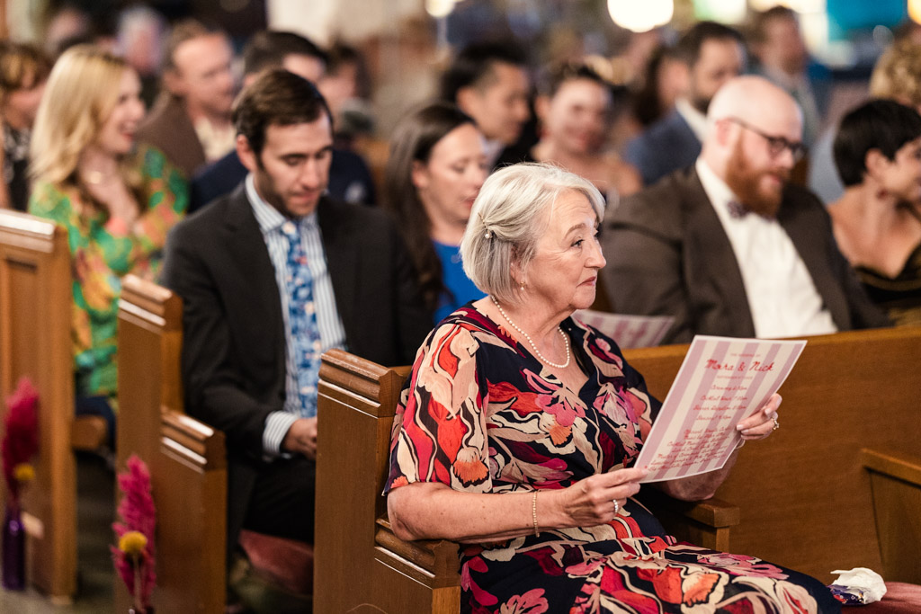 Guest holding a program, seated among others in a church pew during a Salvage One wedding