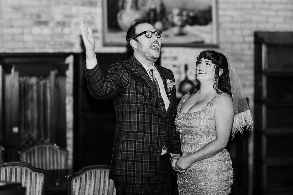 Black and white photo of groom singing while the bride looks on and holds his hand during their Salvage One wedding ceremony
