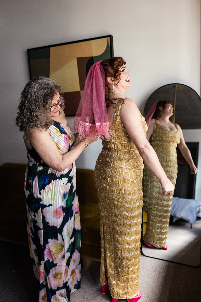 Bride's mother helps bride in a gold dress and pink veil get ready at the Emily Hotel before her Salvage One wedding
