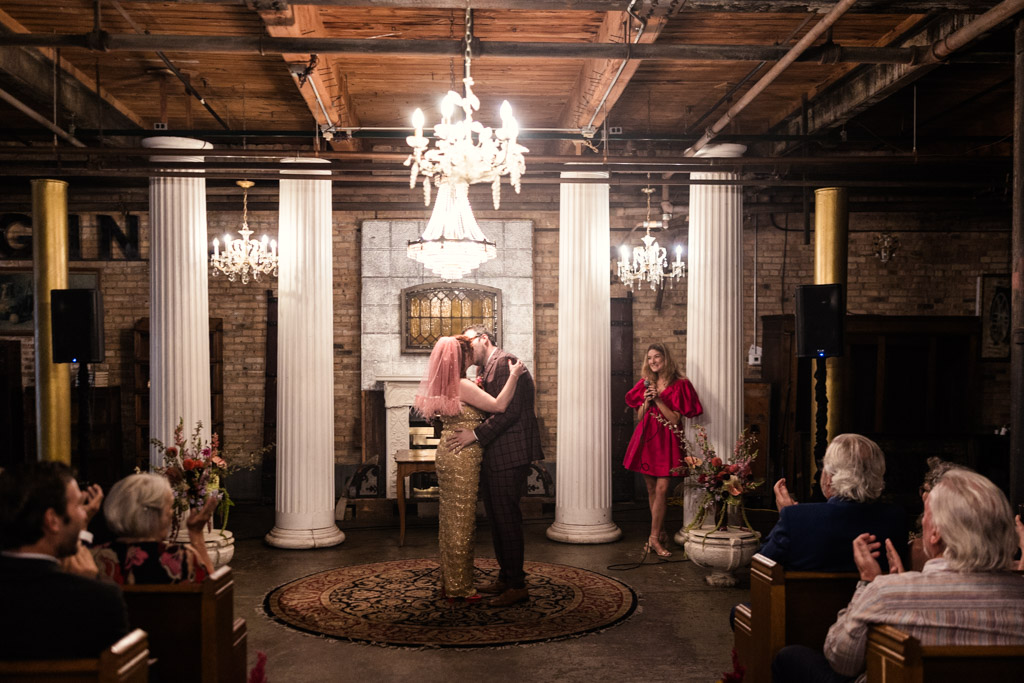 Newlywed couple kisses at their Salvage One wedding ceremony as guests watch and applaud