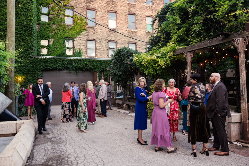 Guests in colorful attire gather and chat in a ivy-covered outdoor courtyard during Salvage One wedding reception