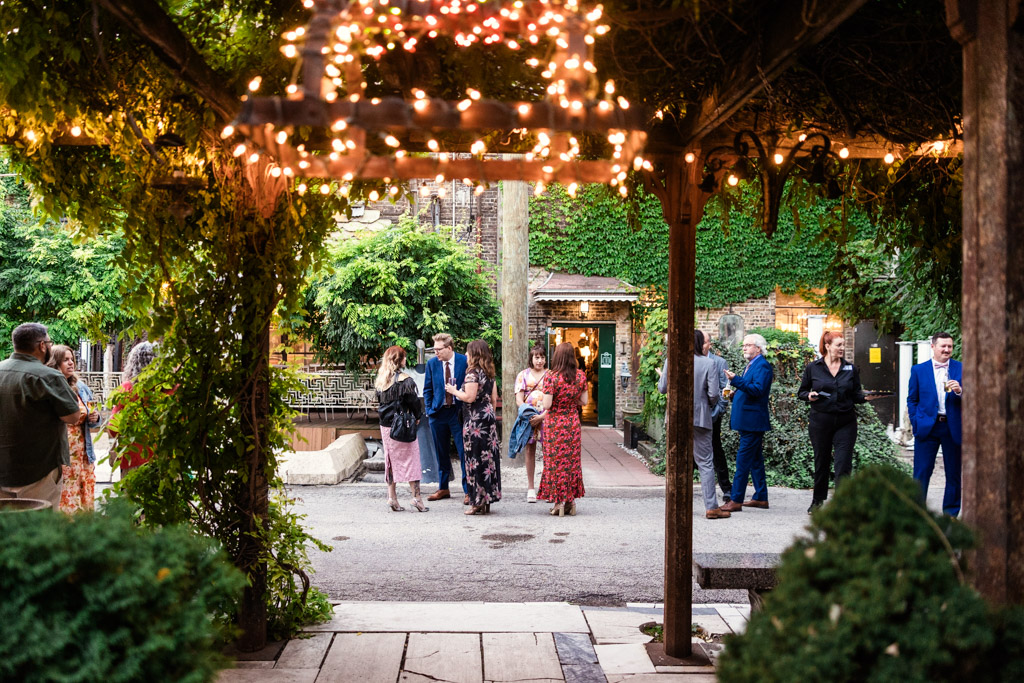 Guests dressed formally gather outdoors under string lights and greenery at a Salvage One wedding reception