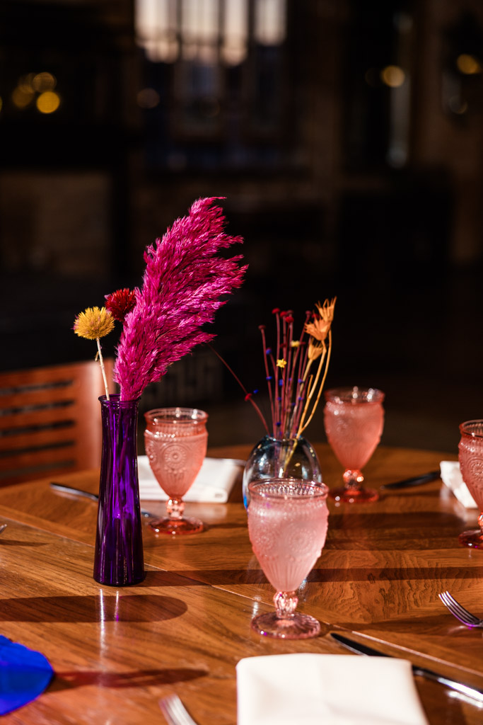 Pink drinks and vintage glasses on a guest table with colorful dried flowers in vases as centerpieces for Salvage One wedding reception