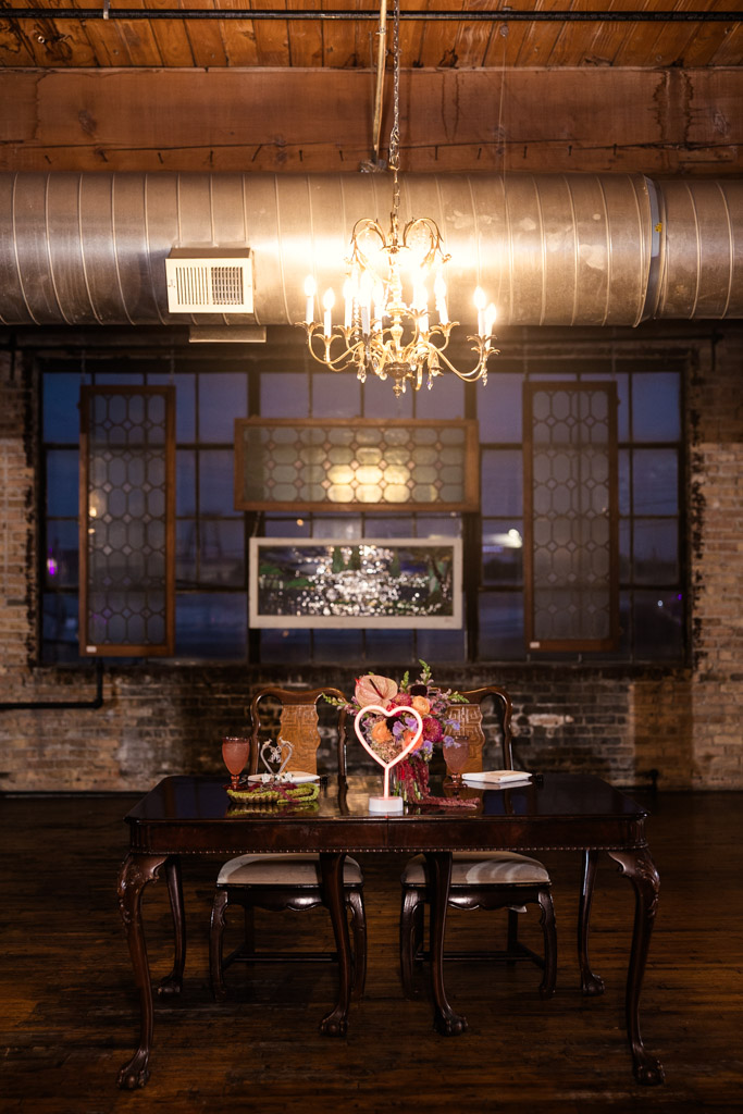 Sweetheart table under a chandelier in an industrial-style room with large windows at Salvage One wedding reception