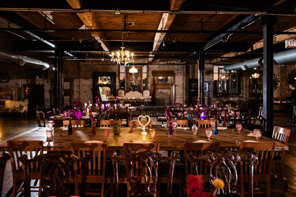 Salvage One wedding reception space with wooden tables, ornate chairs, chandeliers, and dim, warm lighting