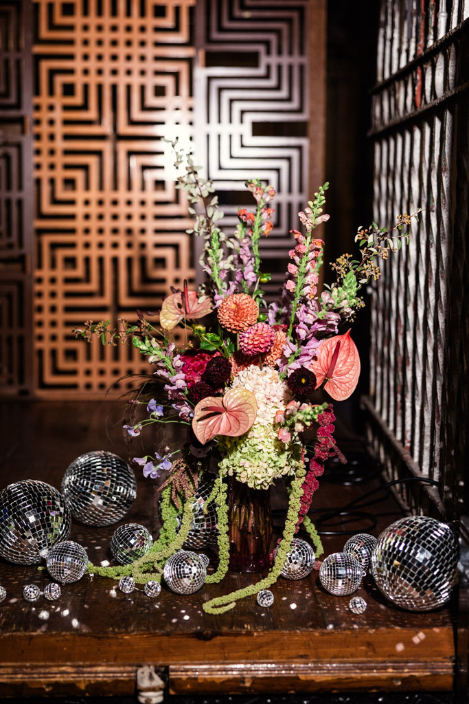 A colorful flower arrangement with disco balls sits on a wooden table against a geometric patterned wall at Salvage One wedding celebration