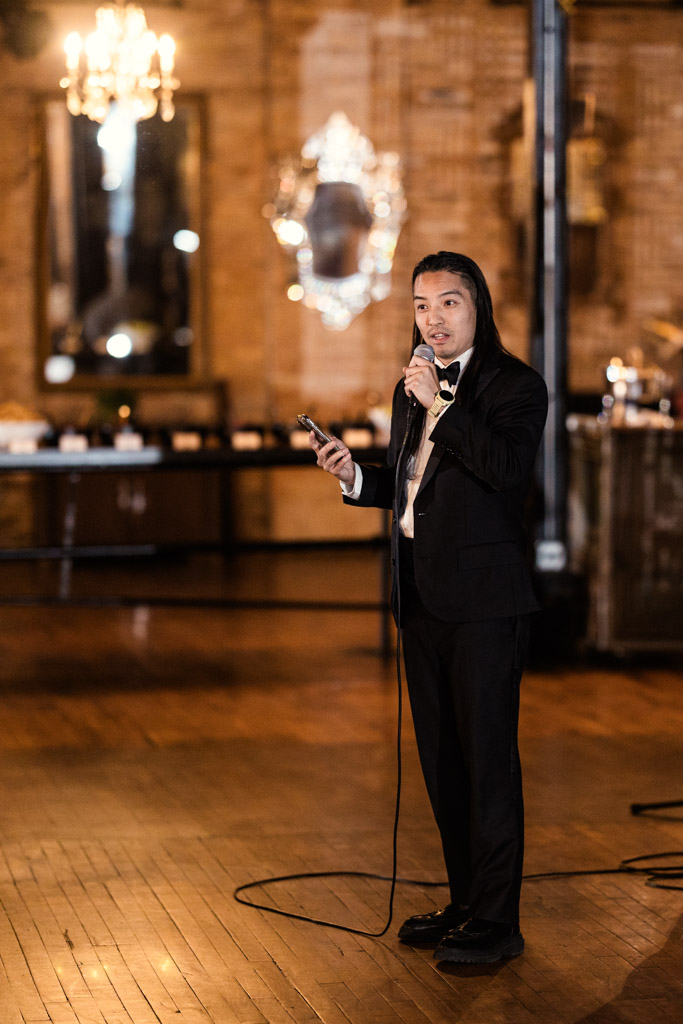 Guest in a black suit gives speech at Salvage One wedding reception
