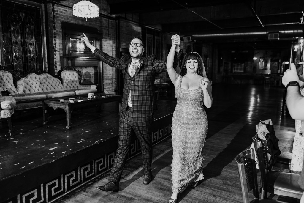 Black and white photo of joyful newlywed couple in formal attire holding hands while entering their Salvage One wedding reception