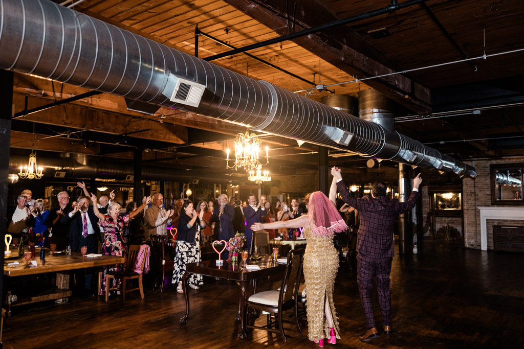 Newlyweds raise their hands and enter their Salvage One wedding reception as guests cheer