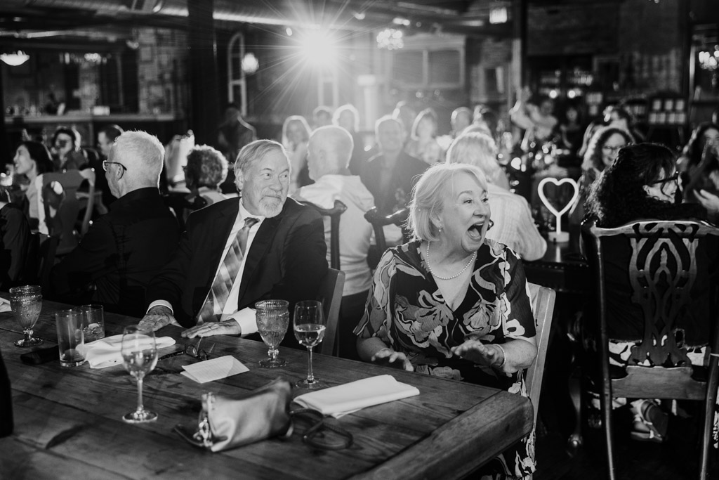 Groom's mother laughs during Salvage One wedding reception, surrounded by seated guests at dining tables
