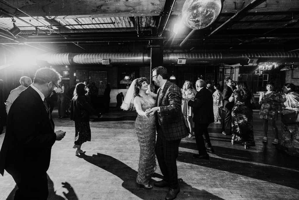 Black and white photo of bride and groom dancing together on a lively, crowded Salvage One wedding reception dance floor