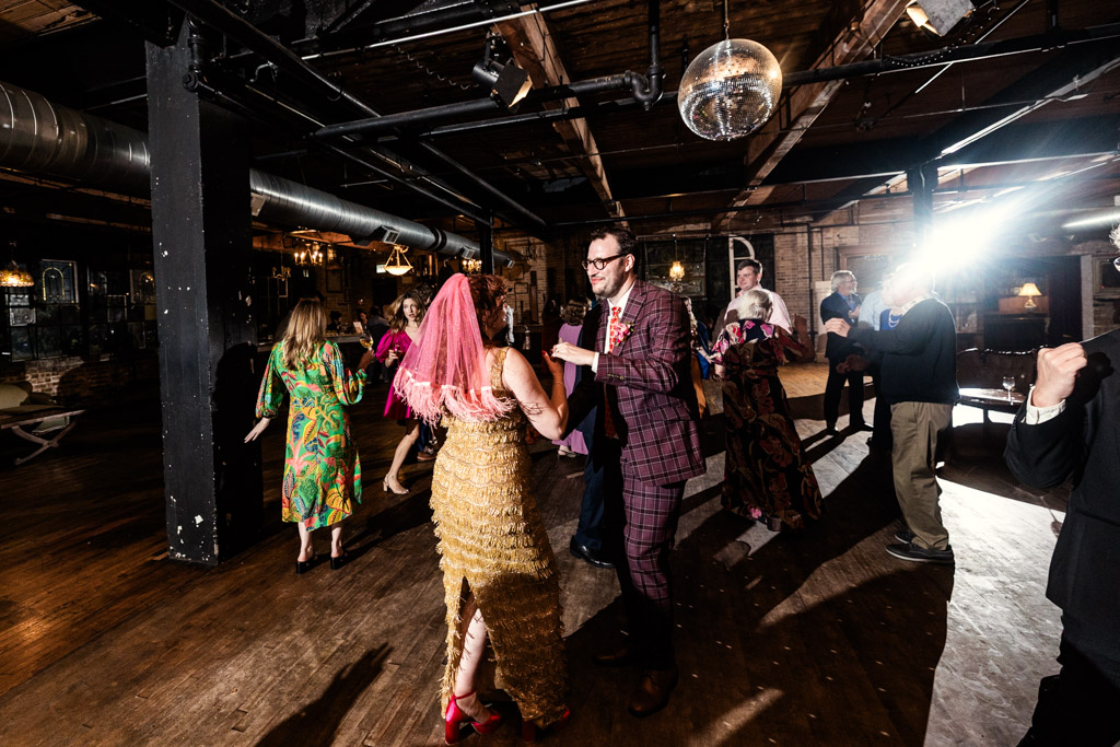 Bride and groom dancing in a dimly lit venue with wood floors and a disco ball overhead during Salvage One wedding celebration