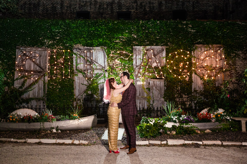 Photo of newlywed couple embracing in front of a lit 