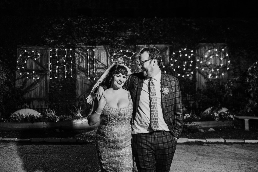 Candid black and white photo of smiling bride and groom walking arm-in-arm at night after their Salvage One wedding, with 