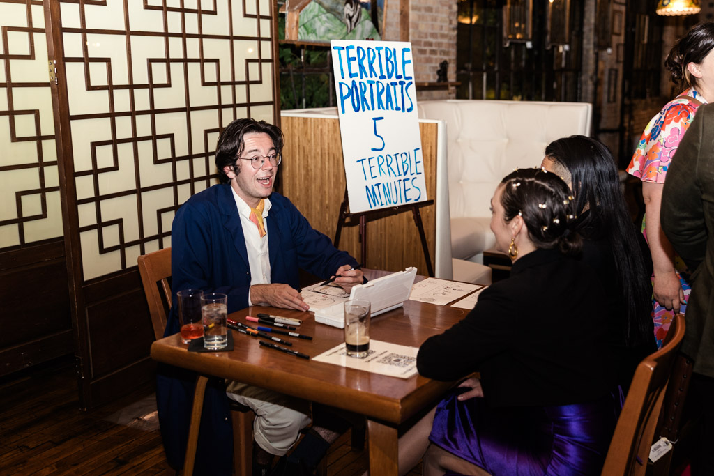 A man draws portraits at a table with a sign reading 