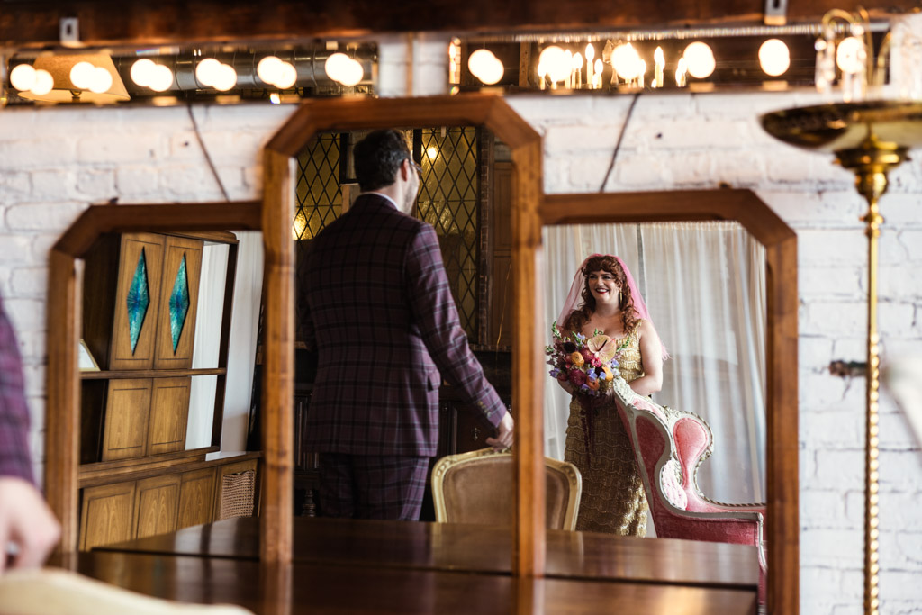 Creative photo of bride holding a bouquet smiling at her groom, both reflected in a vintage mirror during their Salvage One first look