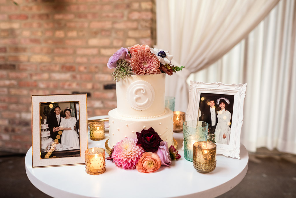 A white cake with flowers, surrounded by candles and framed wedding photos for wedding reception at The Arbory Chicago