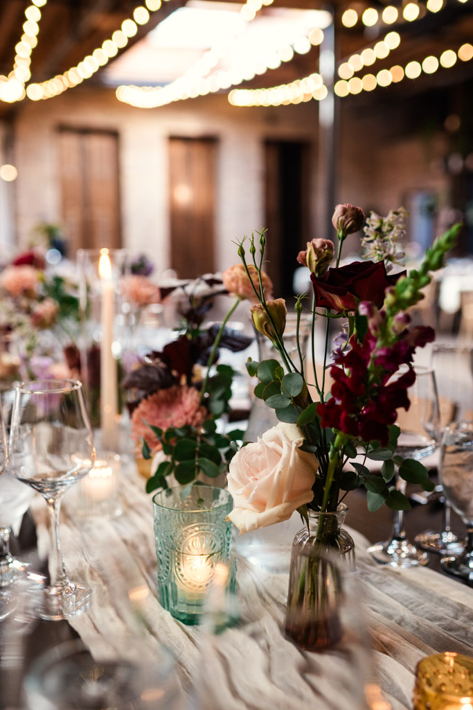 Guest table setting with flowers, candles, and wine glasses under string lights in the wedding reception space of The Arbory Chicago