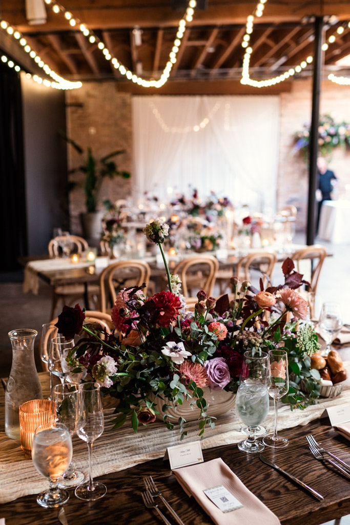 Guest table with floral centerpiece, candles, glassware, and string lights for Arbory Chicago wedding reception