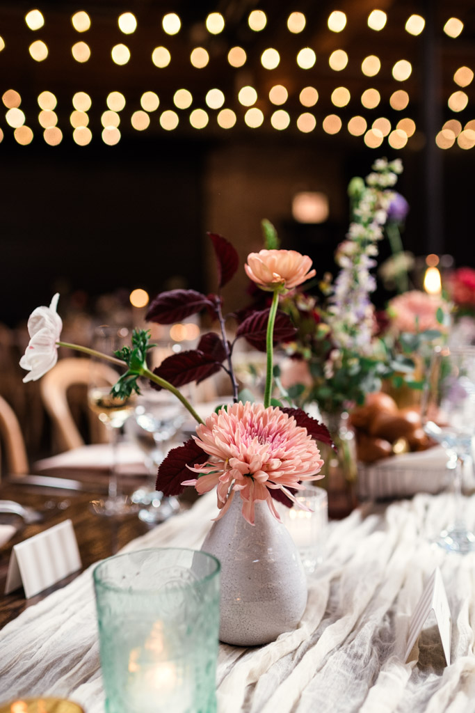 Vase with pink flowers on a wedding reception guest table at The Arbory Chicago, with string lights blurred in the background