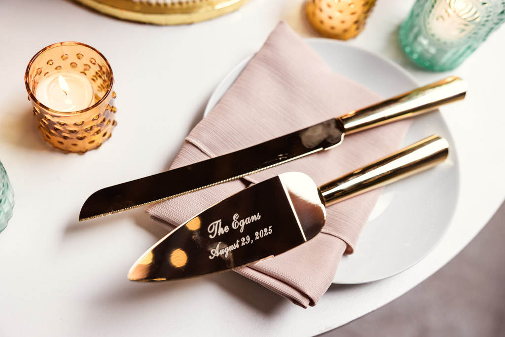 Custom engraved gold cake knife and server on a plate and napkin beside candles for wedding reception at The Arbory Chicago