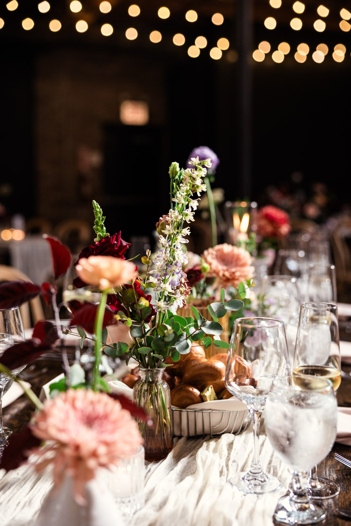 Guest table setting with flowers, glassware, and bread under string lights in wedding reception space at The Arbory Chicago
