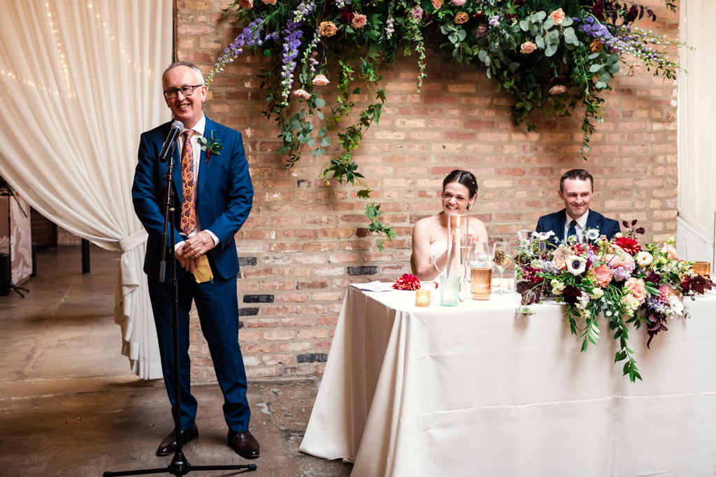 Groom's father gives a speech at a wedding reception at The Arbory Chicago as the bride and groom smile at the head table