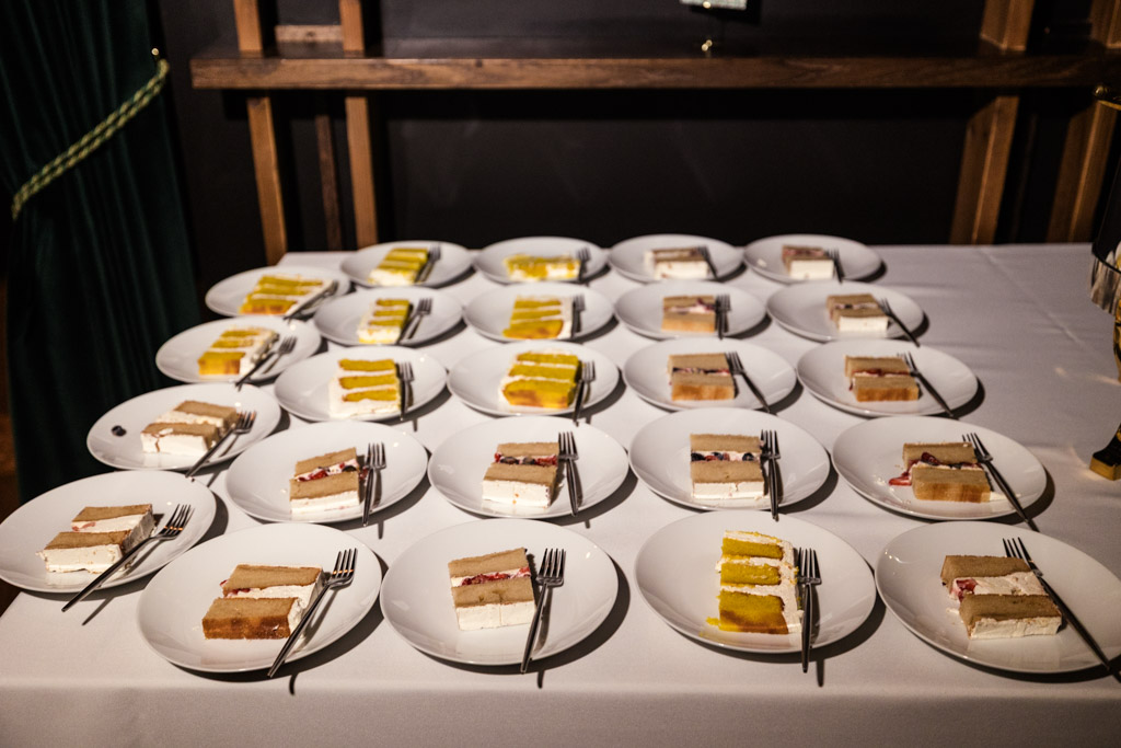 Rows of plates with assorted slices of cake and forks are arranged on a white tablecloth for wedding reception at The Arbory Chicago