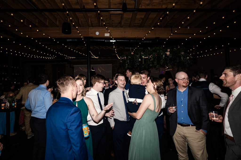 Guests dressed formally chatting and laughing under string lights during wedding reception at The Arbory Chicago