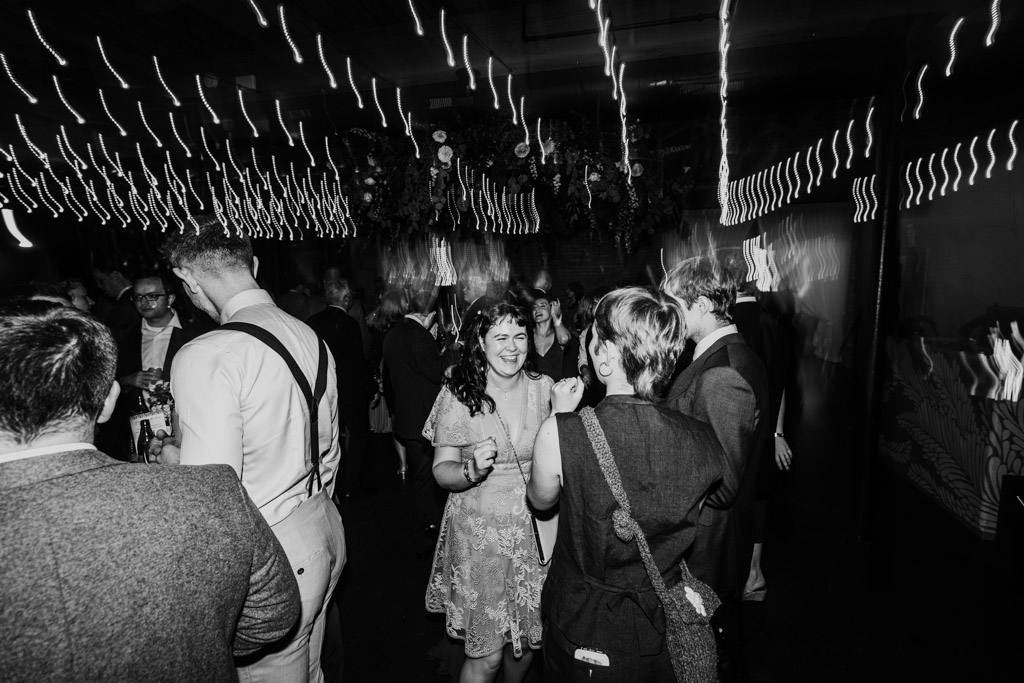 Black and white photo of guests in formal wear dancing and mingling under string lights during wedding reception at The Arbory Chicago