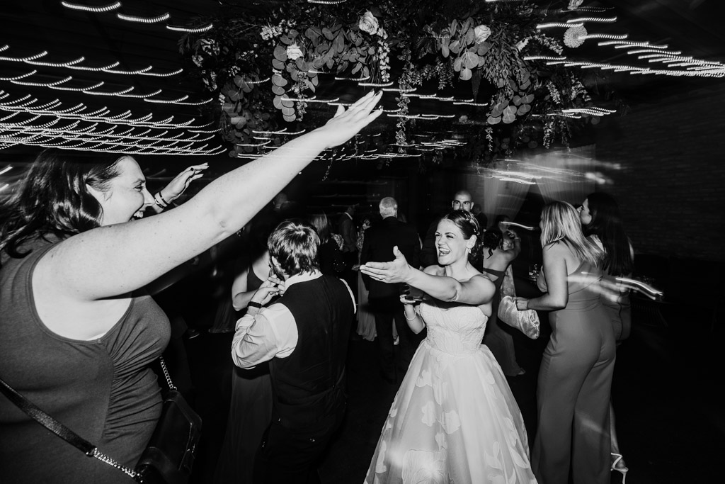 Creative black and white photo of bride in a white dress dancing with guests during her wedding reception at The Arbory Chicago
