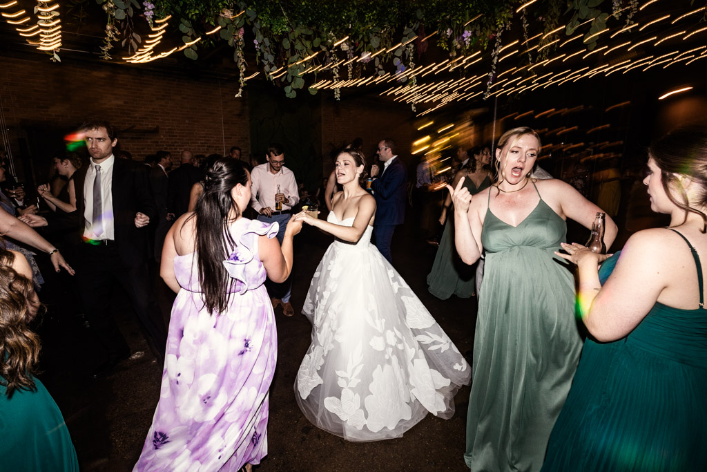 Bride in white and guests dance under string lights during wedding reception at The Arbory Chicago