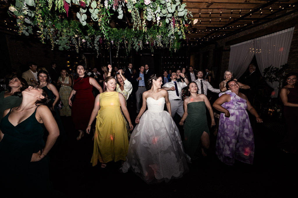 Bride and guests dance under hanging greenery and string lights at The Arbory Chicago wedding reception