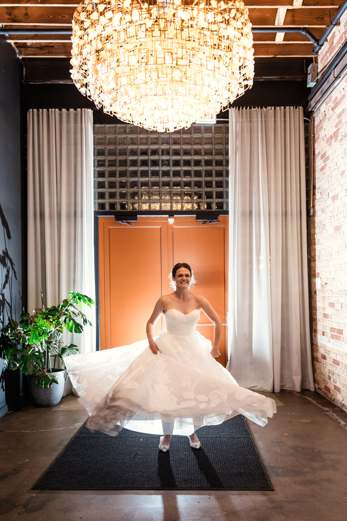 Bride in a white dress twirls under a large chandelier in a stylish, modern room at The Arbory Chicago