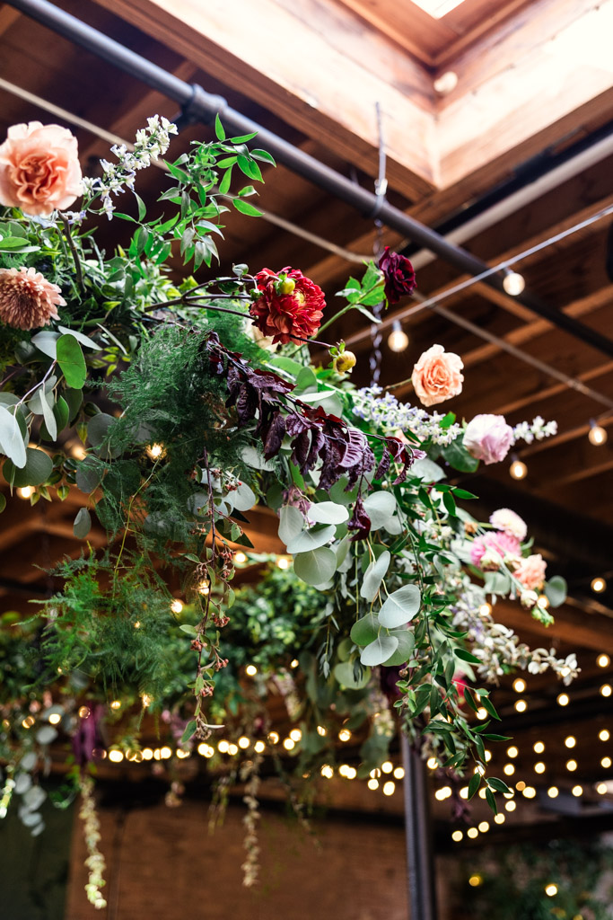 Floral arrangement with roses and greenery hanging under string lights in wedding ceremony space at The Arbory Chicago