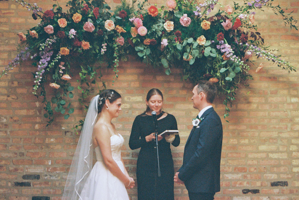 Film photo of bride and groom standing before an officiant under a floral arrangement during their wedding ceremony at The Arbory Chicago
