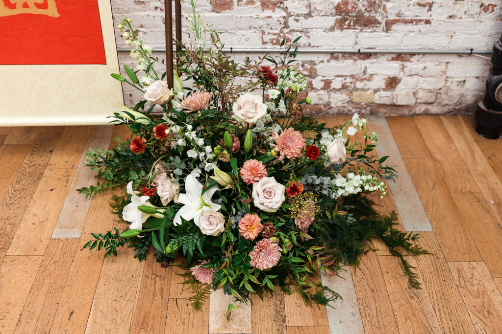 Floral decor with roses, lilies, and greenery sits on a wooden floor against a brick wall for wedding ceremony at The Joinery in Chicago