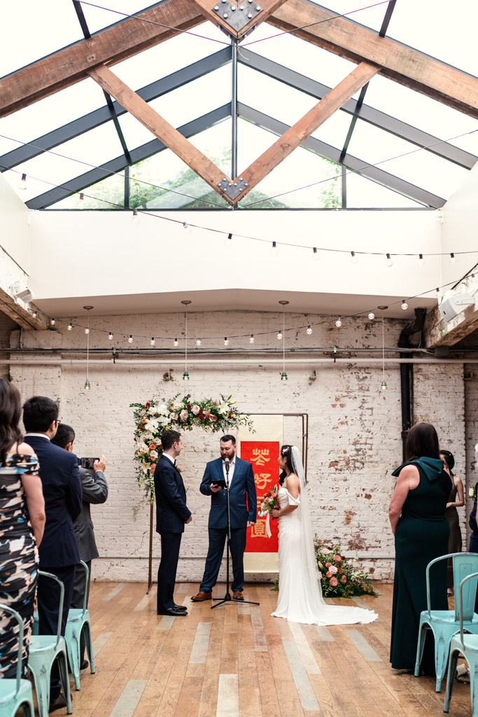 A couple stands under a floral arch during their wedding ceremony at The Joinery in Chicago