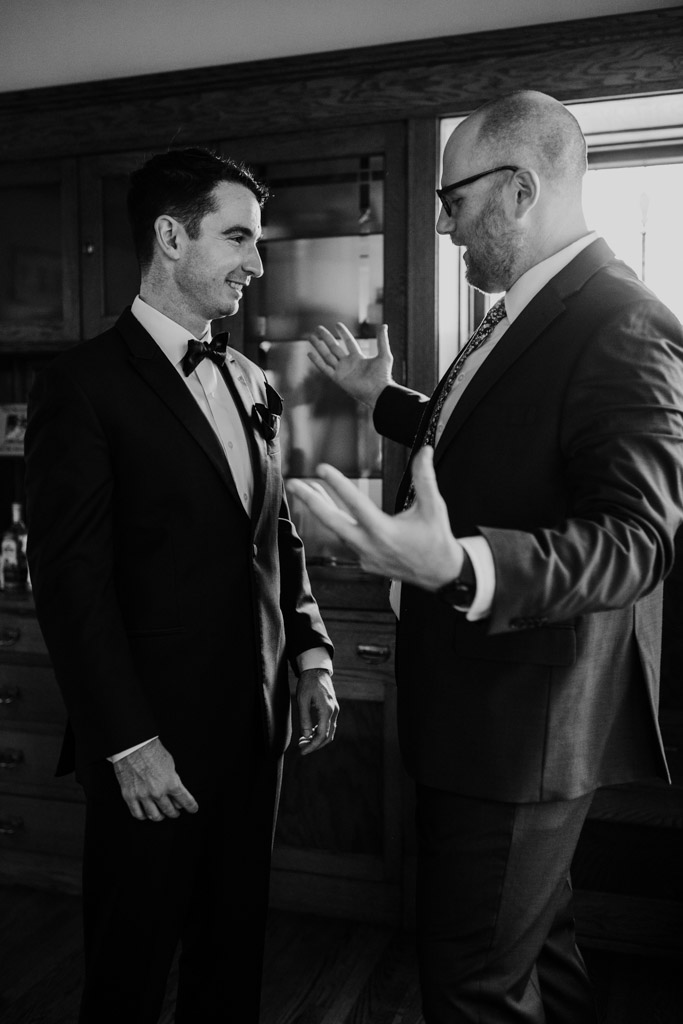 Candid black and white photo of groom and groomsman talking to each other before a wedding celebration at The Joinery in Chicago
