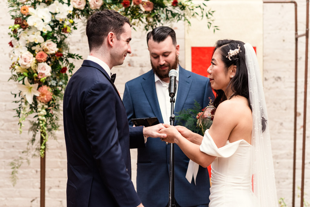 Bride and groom holding hands during their wedding ceremony at The Joinery in Chicago, framed by a floral arch with the officiant behind them
