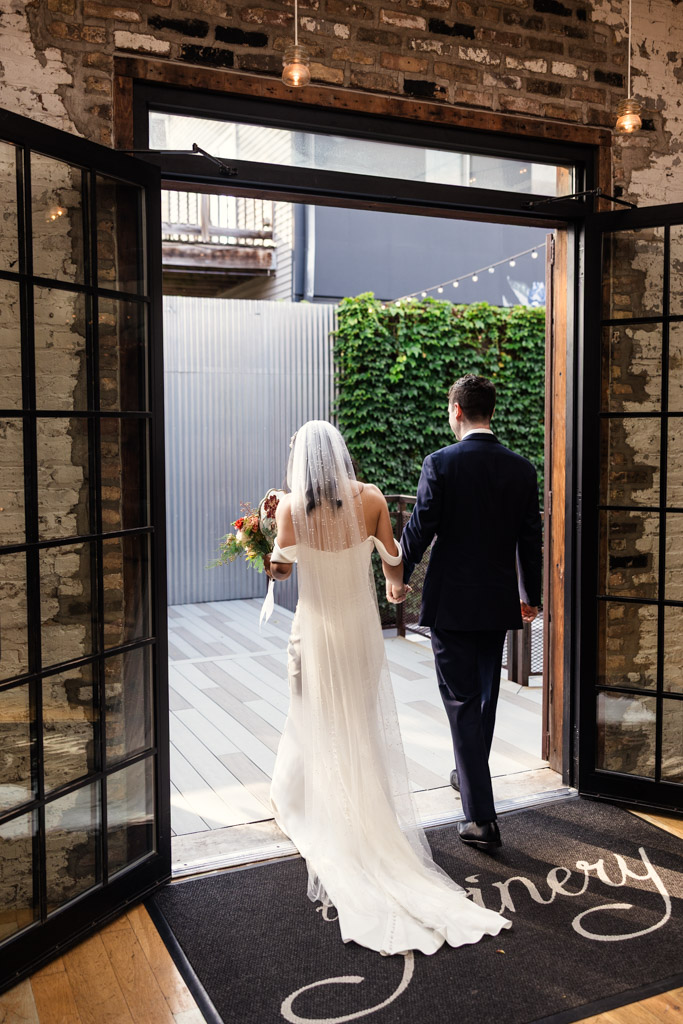 A bride and groom walk hand in hand toward an outdoor patio after their wedding ceremony at The Joinery in Chicago
