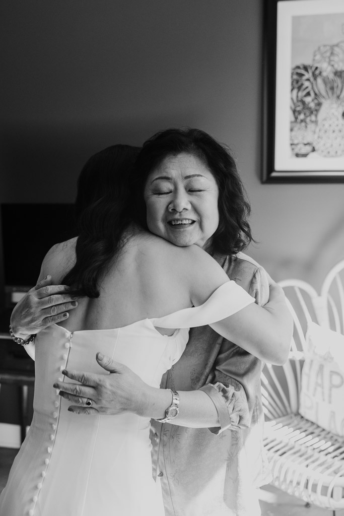 Black and white photo of bride in a wedding dress hugging her mother while getting ready for her wedding celebration at The Joinery in Chicago