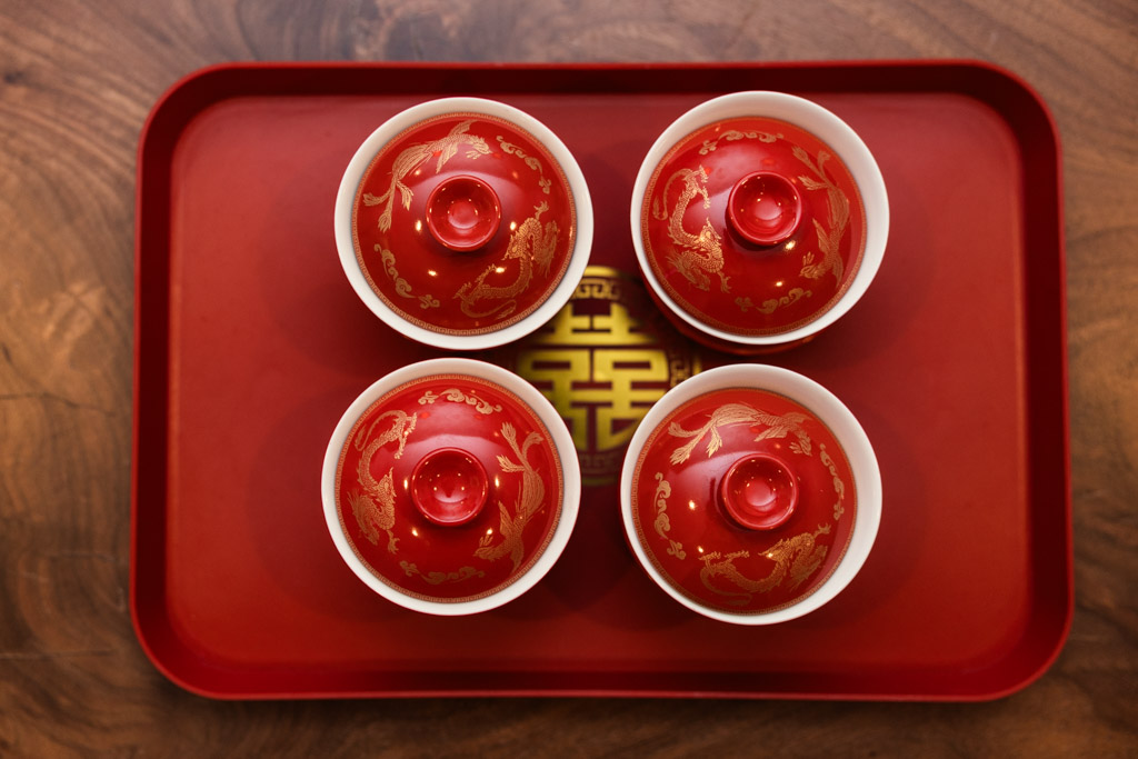 Four red Chinese tea cups with lids rest on a red tray, viewed from above