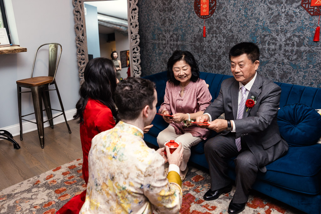 Bride and groom exchange red envelopes with bride's parents during a traditional tea ceremony