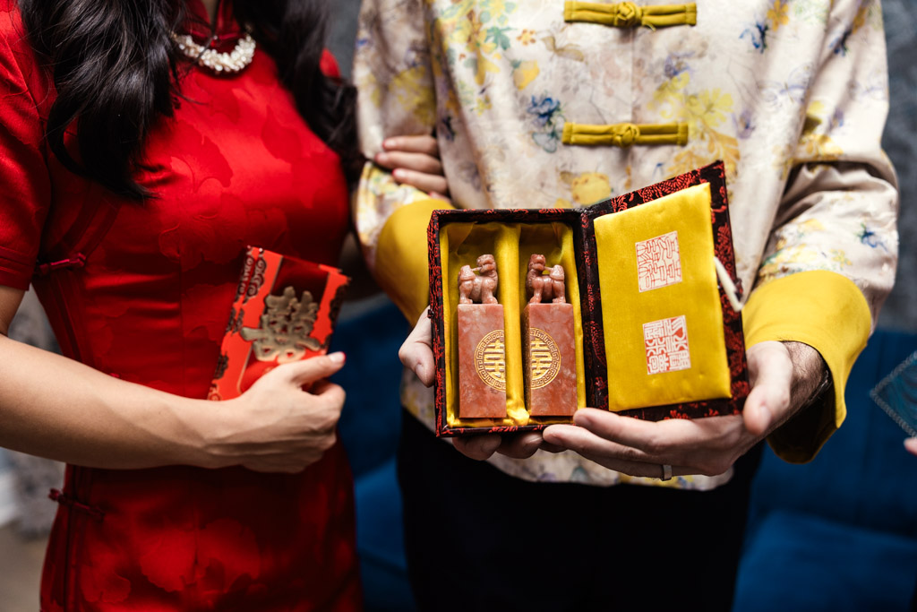 Bride and groom in traditional Chinese attire hold a box with two red seals after tea ceremony