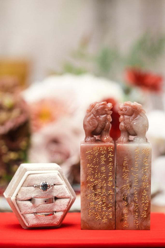 Two hand-carved stone seals with gold inscriptions and a jewelry box holding rings, set on a red surface for wedding celebration at The Joinery in Chicago