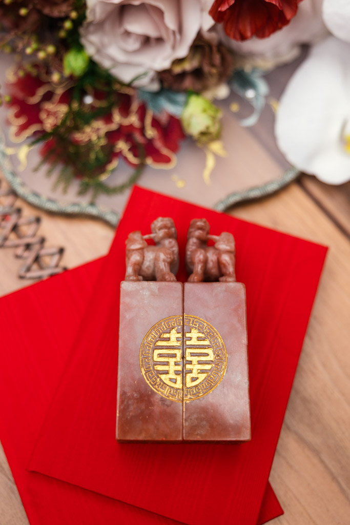 Two red stone seals with gold double happiness symbols rest on red envelopes, surrounded by flowers for wedding celebration at The Joinery in Chicago