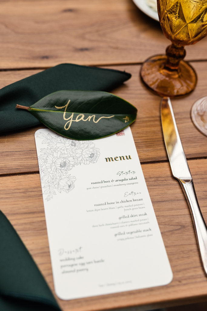 Bride's place setting with wedding menu on a wooden table with amber glass, and a custom name leaf at The Joinery in Chicago