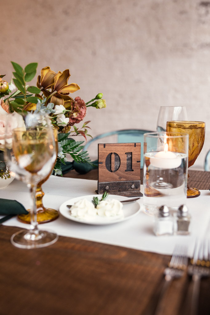 Guest table setting with flowers, glassware, a wooden table marker for wedding reception at The Joinery in Chicago